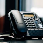 Un telefono fisso nero è appoggiato ad una scrivania d'ufficio